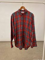 Front full view of the vintage Christian Dior plaid flannel shirt hanging on wooden hanger, showing pattern and buttons.