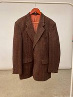 Full front view of brown Harris Tweed sports coat hung on wooden hanger showing classic cut and button closure.