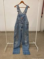 Full view of vintage IKEDA denim overalls on hanger showing overall shape and color.