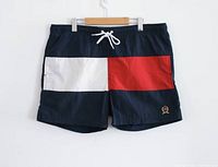 Front view of vintage Tommy Hilfiger swim shorts featuring large red, white, and navy flag and embroidered logo