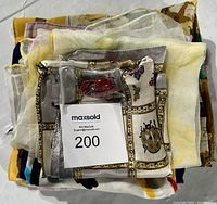 Folded pile of various silk scarves along with plastic bag containing the brooch