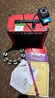 Photo showing red amplifier, black tambourine, pink recorder, and several music books and sheet music tipped on carpet.