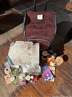 Wide shot showing large wheeled craft storage case, bead storage boxes, assorted beads, ribbons, threads, books, and bead accessories.