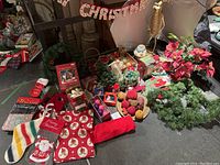 Overview of multiple Christmas decorations including stockings, garland, ornaments, and banners on floor with photography reflector in background.