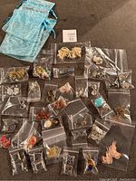 Full view of 32 pairs of cosmetic clip-on earrings arranged on table in small zip bags along with 4 decorative blue gift bags.