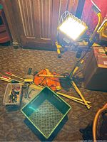 Overview of lot items including work light, safety vest, boxes, and tools on carpeted floor.