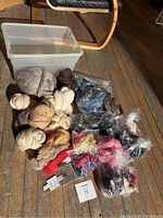 Various felting fibres in open packages and bunches in assorted colors, plastic storage bin with lid, and a set of assorted felting needles laid on wooden floor with chair nearby.