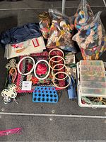 Crafting supplies laid out on floor: assorted threads in bags and plastic containers, embroidery hoops, navy fabric bag, scissors, yellow tool, thread holders and floral patterned fabric pieces.