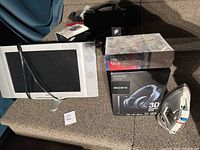 Overview photo of the lot showing TV, Sony Headphones in box, Corel WordPerfect software box, and iron placed on a grey surface.