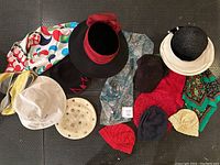 Photo of 11 hats including formal black hat, knitted berets and toques, ball cap, and black sun hat, with colorful scarves underneath and beside them.