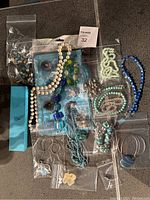 Overview of 10 necklaces, earrings and bracelets in plastic bags displayed on dark surface