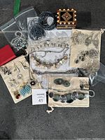 Overview of assorted jewelry laid on a grey surface showing necklaces, rings, earrings, brooches, bracelet, trinket box, and gift bags.