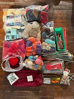 Photo showing multiple bundles of assorted yarn in various colors and types, knitting needles, crochet hooks, needle tools, and storage containers.