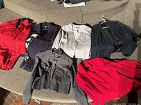 Display of multiple ladies jackets in varied colors including red, grey, navy, and black, arranged on carpet showing variety in style and fabric