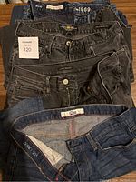Stacked front view of four pairs of men's jeans showing waistbands and button details including labels and size tags