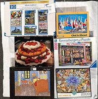 Six boxed jigsaw puzzles shown arranged on white sheet. Boxes depict puzzle images and piece counts. Various sizes and styles visible.