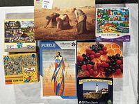 Photo showing six jigsaw puzzle boxes of various themes and sizes laid out on a white surface for identification and documentation.