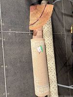 Photo showing three rolled rugs including a beige runner with a geometric pattern and two other rugs with various patterns.