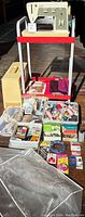 Full view of sewing machine setup on red wheeled cart with cover, assorted sewing supplies in front including threads and accessories organized in trays.