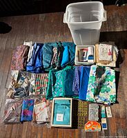 Full overview of all contents including fabrics, patterns, and sewing accessories laid out on the floor with white plastic storage bin.