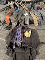 Three men's suits displayed with matching ties and silk handkerchiefs on a couch.