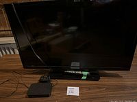 Full view of the 33-inch Insignia TV on a wooden surface, showing the TV screen, stand with remote, and Mag box device connected via cable.