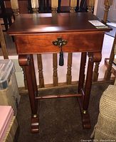 Front angled view of the wooden side table showing drawer with brass handle and tassel, curved legs, and stretcher bar.