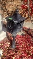 Full view of freestanding cast iron mailbox on pedestal, showing roof lid, relief panel and base.