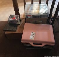 Photo of all items including pink and transparent cassette tape storage cases, CDs stacked on a wooden box, and miscellaneous items.