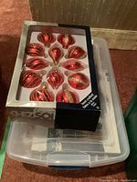 Box of red and gold hand-crafted glass tear drop Christmas tree ornaments resting on plastic storage container