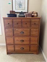 Front view of wooden dresser with 4 drawers, showing mixed drawer pulls and decorative items on top.