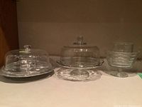 Three glass servers displayed in one image, two cake stands with covers and a pedestal condiment server.