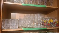 Shelf showing multiple clear crystal and stemmed glasses and colorful fruit-printed cocktail glasses
