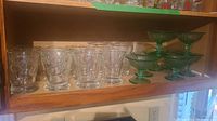 Shelf with 9 clear floral etched glasses and 5 green stemmed dessert or cocktail glasses.
