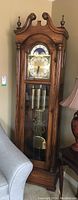 Full view of tall grandfather clock showing wood finish and glass front door exposing weights and pendulum.