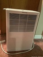 Front view of Hisense white dehumidifier with air vents and power cord visible on carpeted floor.