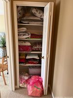 Closet with shelves containing neatly folded assorted linens, towels, and pillow covers; two pink plastic bags resting at the bottom of the closet.