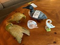 Tabletop display of five bird figurines: carved wood loon, Lladro swan, glass swan, and two brass birds
