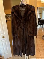 Full-length front view of long dark brown mink fur coat on hanger