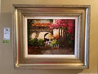 Framed painting of a sunlit outdoor patio with archways, table, parasol, and flowers.