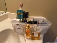 Clear plastic bin on sink holding multiple fragrance bottles and a decorative tin