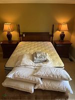 Front view of complete lot showing wood headboard, mattress on box spring on frame, folded bedding on mattress and pillows on floor.