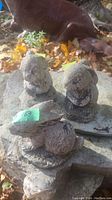 Photo showing three small concrete rabbit garden statues placed on uneven stone surface amidst fallen autumn leaves and an outdoor background.