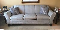 Front view of gray fabric three-seat sofa with two matching throw pillows