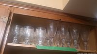 Eight pieces of clear glass stemware, four goblets and four smaller glasses, arranged on a wooden shelf.
