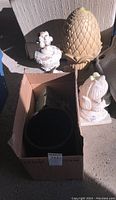 Five yard decorations grouped together including pot in box, bird house, tall pinecone finial, urn with floral top, and abstract sculpture
