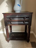 Full view of antique Victorian hardwood side table showing two drawers with wooden knob pulls, turned front legs, and an open bottom shelf. Wood has dark finish and visible wear.