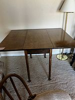 Front view of the walnut table fully extended showing top and legs, standing on a carpeted floor beside a lamp and chair.
