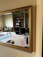 Front view of large gilt-framed mirror mounted on wall, showing reflection of room.