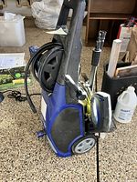 Side view of Blue Clean AR383 electric power washer showing handle, wheels, hose reel, and attached spray gun.